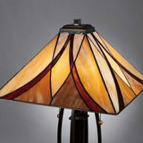 The Asheville 2 Light Tiffany Table Lamp - Valiant Bronze features a classic Tiffany-style shade in warm hues of orange, yellow, and red that sits elegantly against a plain gray background, with its base finished in Valiant Bronze.
