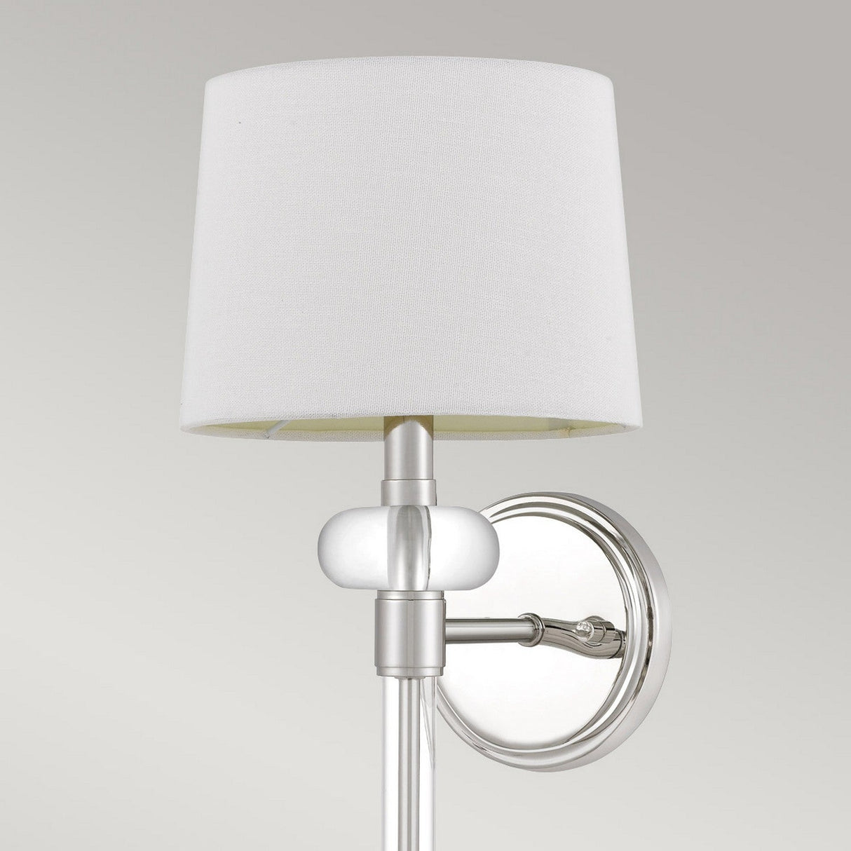 Introducing the Barbour 1 Light Wall Light in polished nickel. This wall-mounted fixture features a polished metal base and a white fabric lampshade. It showcases a round backplate and a sleek arm design, effortlessly merging modern decor with classic elements. Perfect for adding ambient light to its plain gray backdrop.