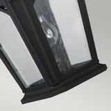A close-up view of the Bedford Outdoor 1 Light Large Wall Lantern in black highlights its clear glass pane, dotted with raindrops. The visible light bulb inside is framed against a neutral gray background.
