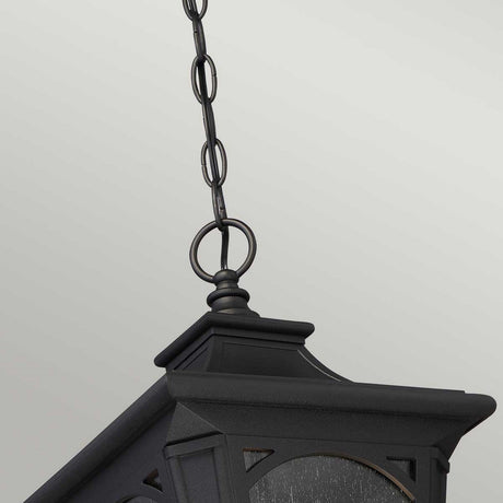 The Bedford Outdoor 1 Light Small Chain Pendant - Black, featuring a square shape and peaked top, is elegantly suspended against a light gray backdrop. Its glass panels and black geometric design provide a modern aesthetic, while the inclusion of seedy glass infuses a classic touch into this fixture.