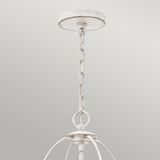 Close-up of the Bradbury 4 Light Chandelier in Antique White, showcasing its rustic hanging light fixture. This four-light design includes a distressed finish, metal loops, and a spherical shape that exudes vintage charm. It is connected to a circular ceiling mount against a plain light grey background.