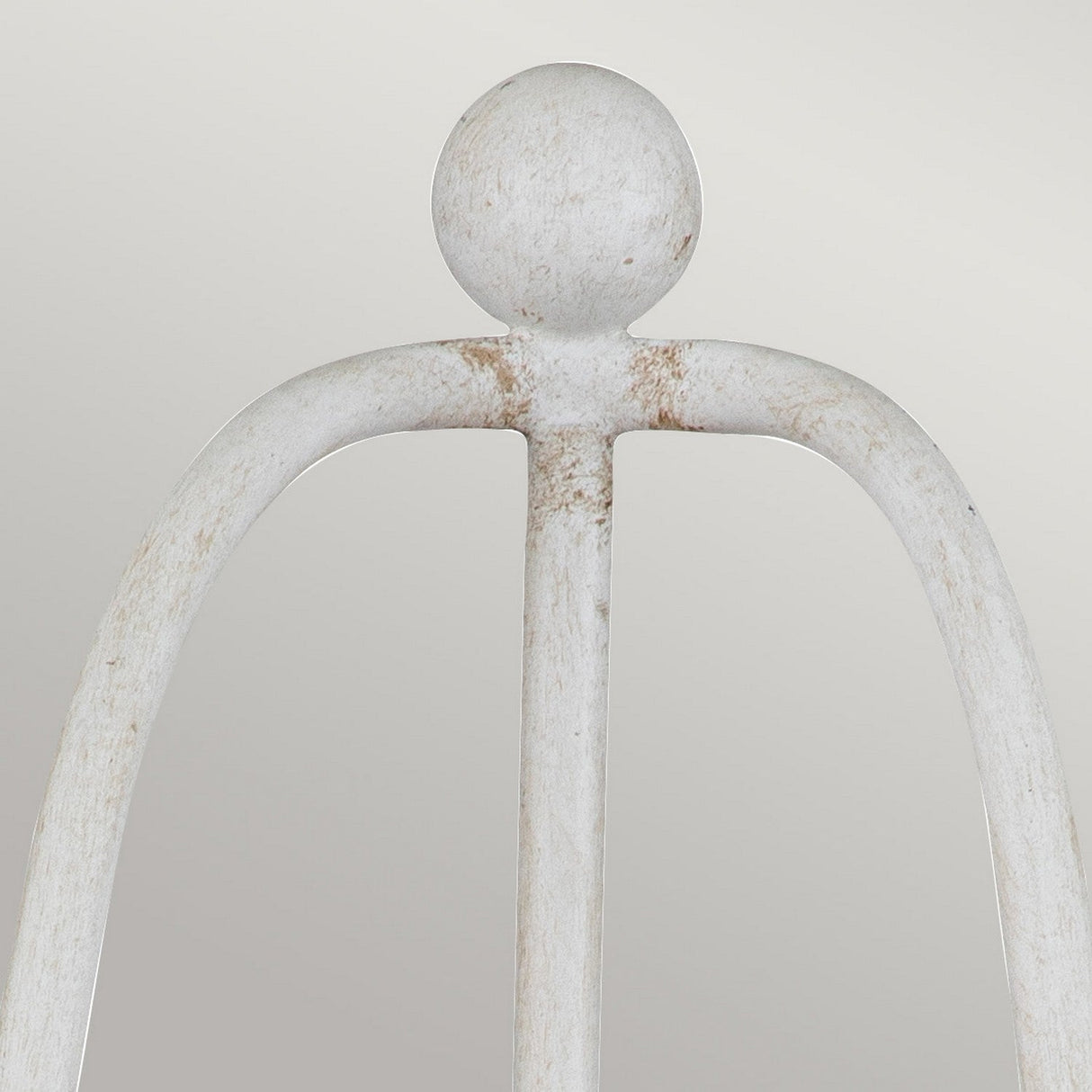 Close-up of the Bradbury 2 Light Wall Light in antique white, featuring a weathered decorative iron design that resembles an abstract figure with a round head and arched arms, set against a plain, light background.