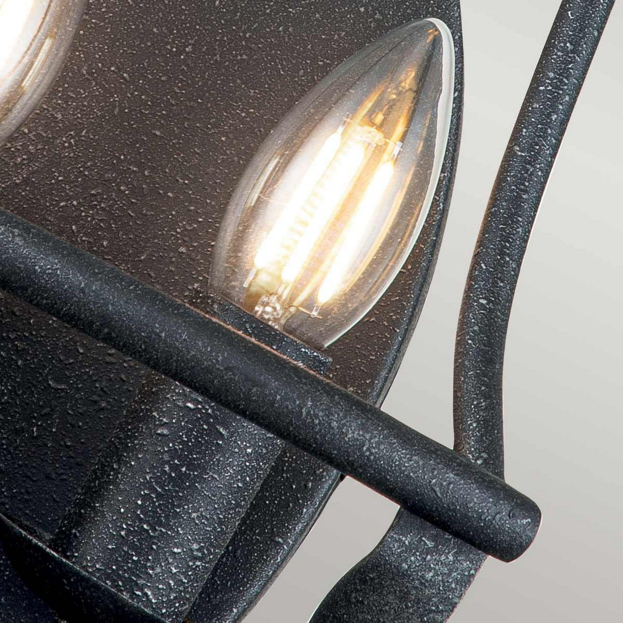 Close-up of the Bradbury 2 Light Wall Light in Grey Ash, featuring a textured metal frame and lit candle-shaped bulbs that showcase its vintage design and warm glow, effortlessly integrating with contemporary design elements.