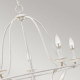 A close-up of the Bradbury 5 Light Chandelier - Antique White showcases its vintage charm, featuring a distressed metal frame and candle-like bulbs, elegantly suspended from a chain against a soft gray background.
