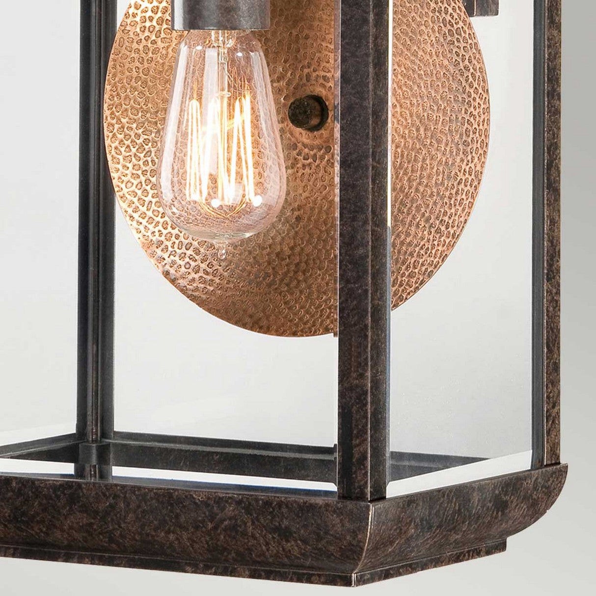 Here is a description using the given product data:

A close-up of the Byron Outdoor 1 Light Large Wall Lantern showcases its vintage-style design, featuring a square metal frame in Imperial Bronze and a clear glass panel. Inside, a glowing filament bulb is mounted against the copper reflector, creating a warm, ambient glow.
