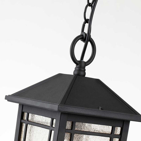 The Cedar Point Outdoor 1 Light Chain Pendant in black showcases rustic elegance with its metal frame and frosted glass design. With seedy glass panels and a pyramid-shaped top, this outdoor chain pendant is highlighted against a light gray background.