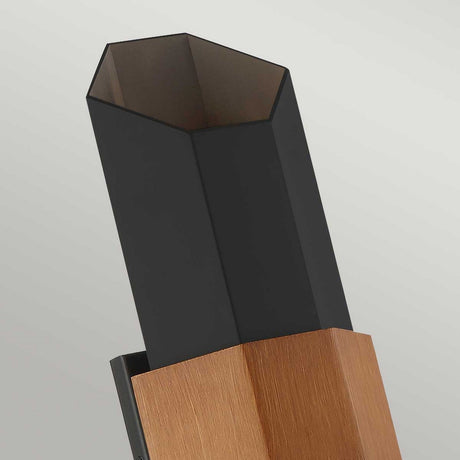 A tall, hexagonal structure featuring a matte black top and a base with a wood-like texture, resembling the elegant Chasm Outdoor LED Large Wall Lantern in Matte Black, set against a neutral background.