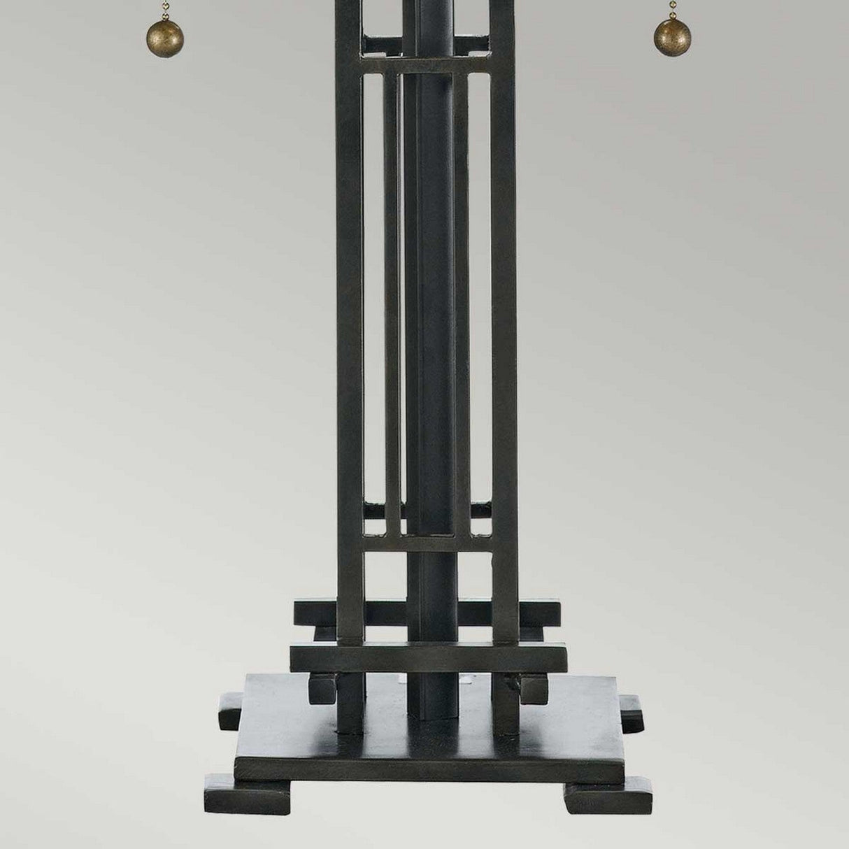 The Chastain 2 Light Tiffany Table Lamp in Vintage Bronze features a geometric design with vertical and horizontal bars on a square base. At the top, two small spheres hang gracefully. The lamp is set against a simple gray gradient background, enhancing its arts and crafts appeal.
