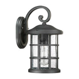 Introducing the Crusade Outdoor 1 Light Medium Wall Lantern in black, featuring an elegant scroll design at the top. This IP44-rated fixture is crafted to withstand the elements and displays clear, textured glass panels that accentuate a visible light bulb inside. Supported by a sturdy metal frame, it exudes a charming rustic appearance ideal for any setting.