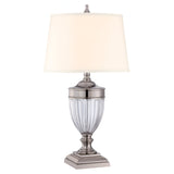 Introducing the Dennison 1 Light Table Lamp - Polished Nickel: a polished silver masterpiece featuring a fluted glass base and a cream-colored lampshade. Resting on a tiered metal pedestal, its polished nickel finish enhances the ambient glow, adding an elegant touch to any decor.