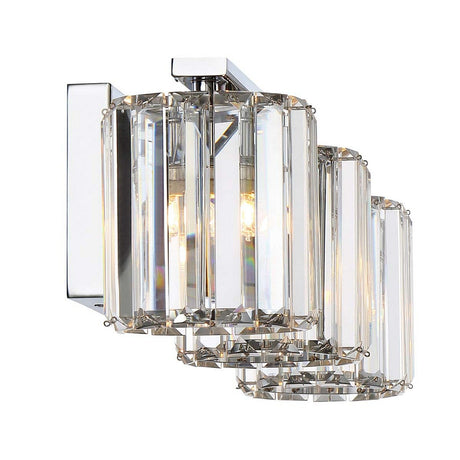 The Divine 3 Light Wall Light - Polished Chrome showcases a contemporary wall sconce design with a polished chrome finish and crystal glass accents. It features three cylindrical glass shades arranged in a linear format, providing bright illumination while maintaining an elegant and sleek appearance.