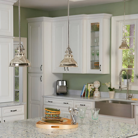 A modern kitchen with sleek white cabinets and a light green wall, featuring an Imperial Silver marble countertop island adorned with a tray of dishes. The space is illuminated by the Emery 1 Light Mini Pendant in Imperial Silver and includes a shiny chrome sink faucet along with an appliance positioned on the counter near a window.