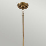 A rustic farmhouse lighting fixture, the Emery 1 Light Mini Pendant - Weathered Brass elegantly attaches to the ceiling with its bronze ceiling rod and decorative round base. Its chain link connection and weathered brass finish lend it a timeless charm, standing vertically against a light gray background.