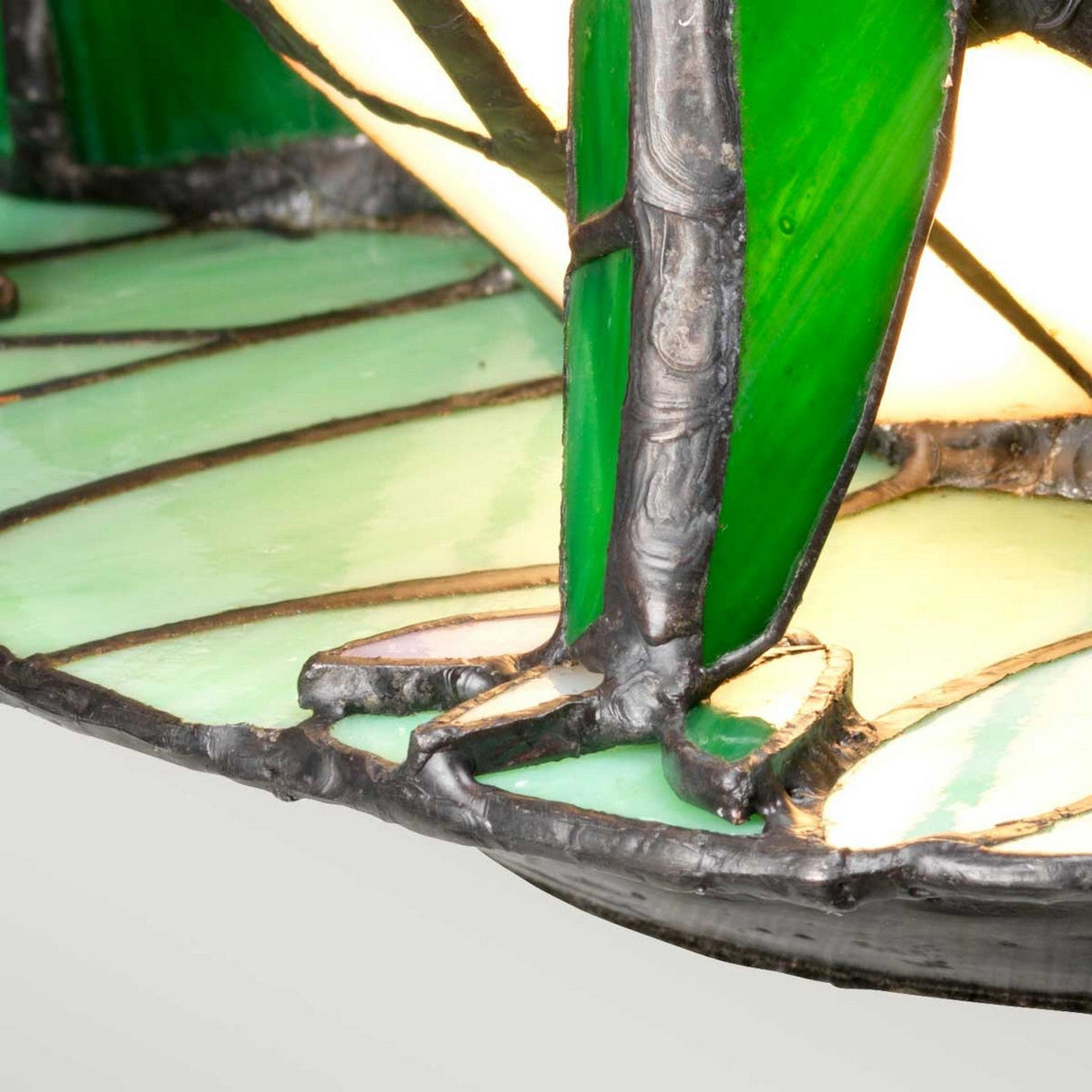 Close-up of the Tiffany Animal Lamps Frog Lamp with intricate green and light yellow stained glass designs, reminiscent of a vintage bronze finish. The metal framework is visible, holding the pieces together, creating an elegant and artistic pattern.