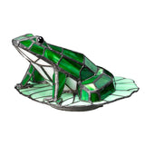 The Tiffany Animal Lamps Frog Lamp in Vintage Bronze showcases a green frog elegantly positioned on a lily pad. The frog is skillfully crafted from green and white glass pieces, with the vintage bronze base highlighting the lighter green elements of the lily pad for an exquisite touch.