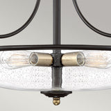 A close-up of the Griffin 3 Light Large Semi-Flush, featuring a clear, textured glass bowl with Edison-style filament bulbs inside. The frame boasts a Palladian Bronze finish with weathered brass accents, set against a plain light gray background.