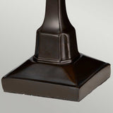 A detailed view of the base of the Holmes 1 Light Mini Tiffany Table Lamp in vintage bronze showcases its sleek, smooth surfaces and angular edges against a neutral light gray background, adding an elegant touch.