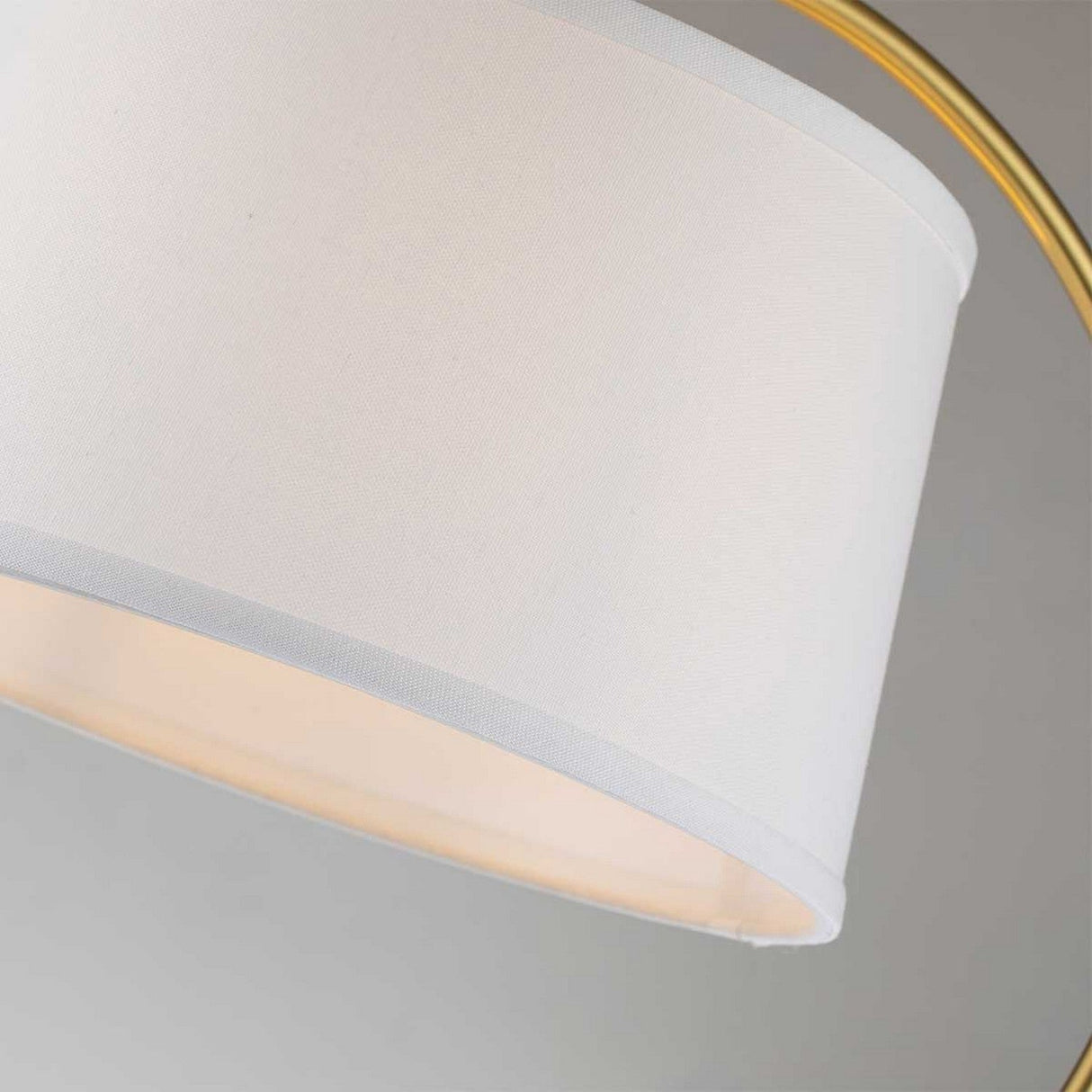 The Jenkins 1 Light Table Lamp - Brushed Brass shines with its modern elegance, showcasing a white linen shade paired with a brushed brass arching frame. Set against a plain gray background, the lamp's sleek and minimalist design is highlighted beautifully.