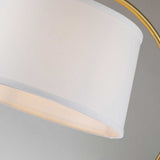 The Jenkins 1 Light Table Lamp - Brushed Brass shines with its modern elegance, showcasing a white linen shade paired with a brushed brass arching frame. Set against a plain gray background, the lamp's sleek and minimalist design is highlighted beautifully.