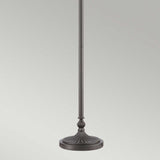 The Kami 1 Light Tiffany Torchiere, in a vintage bronze finish, features a sleek black design with a decorative base that resembles an elegant fluted, shell-like pattern. This lamp includes a round, flat platform at its base and extends vertically upward with a smooth, minimalist aesthetic against a light gray background.