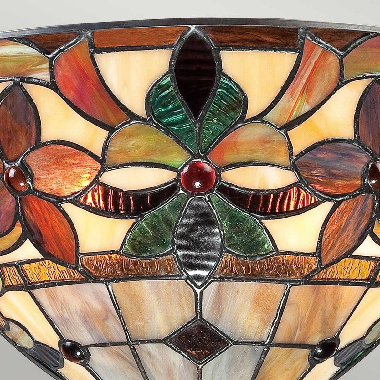 Close-up of a vibrant stained glass lampshade in the style of the Kami 2 Light Tiffany Wall Light - Vintage Bronze, showcasing intricate floral and geometric patterns with shades of red, green, and brown. The design highlights a central flower motif with rich, translucent colors evoking Art Nouveau patterns.