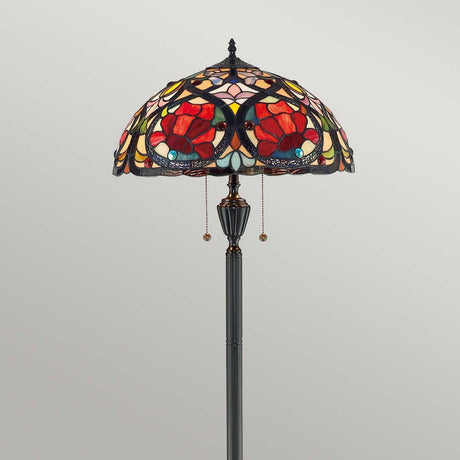 The Larissa 2 Light Tiffany Floor Lamp in vintage bronze highlights a stained glass shade adorned with vivid red and orange poppy designs and geometric patterns. This Art Nouveau masterpiece is supported by an ornate metal stand and comes with two pull chain switches for added convenience.