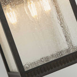 A close-up of the Livingston Outdoor 3 Light Large Wall Lantern - Imperial Bronze reveals its metal frame and textured, seedy glass. Inside, three light bulbs gently cast a warm glow through the glass. The lantern exudes a rustic and weathered charm.