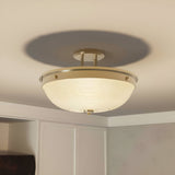 Close-up of the Mantle 2 Light Semi-Flush in weathered brass, featuring prismatic glass and a ribbed, frosted shade that casts a soft glow. Neutral-colored walls surround the space, offering a glimpse of a cabinet below the softly illuminated fixture.