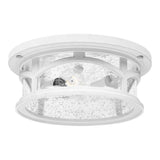 A close-up of the Marblehead Outdoor 2 Light Flush in white, featuring a round design with clear, textured glass panels surrounding the bulb. This weather-resistant lighting piece is designed with decorative accents that resemble windowpanes, allowing visibility of the bulb through the glass.