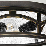 A close-up of the Marblehead Outdoor 2 Light Flush in Palladian Bronze showcases its circular design with clear glass panels, revealing droplets of water on the glass and a partially visible light bulb that creates an illuminated effect.