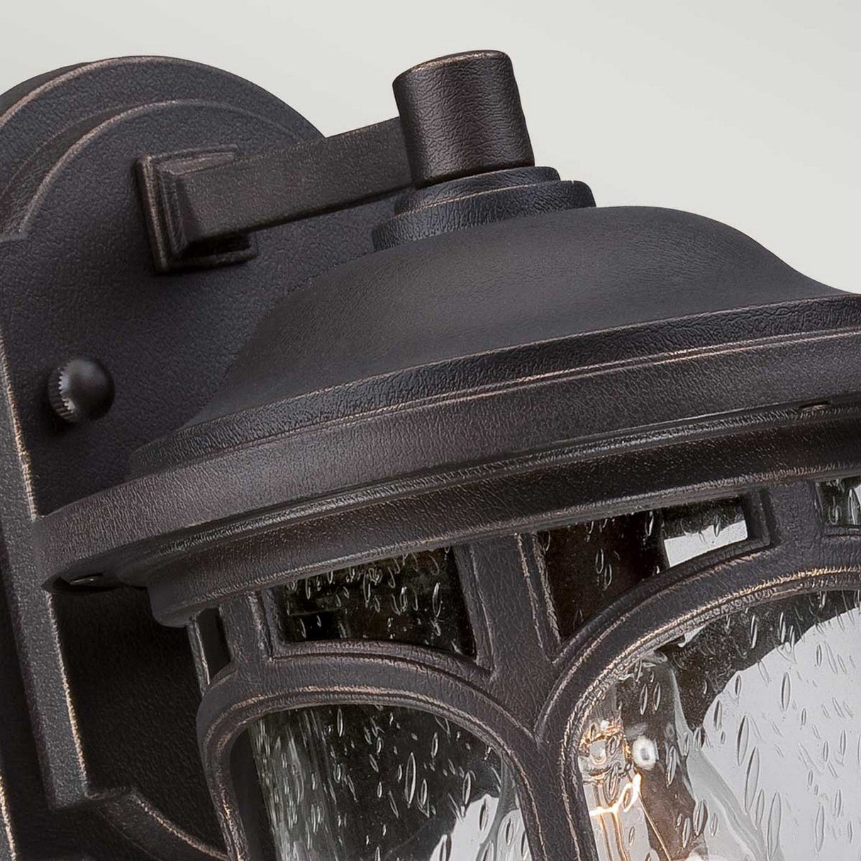 A close-up of the Marblehead Outdoor 1 Light Small Wall Lantern in Palladian Bronze showcases its vintage design. The lantern's seedy glass panels and sturdy metal bracket beautifully enhance the charm of the soft, neutral background.