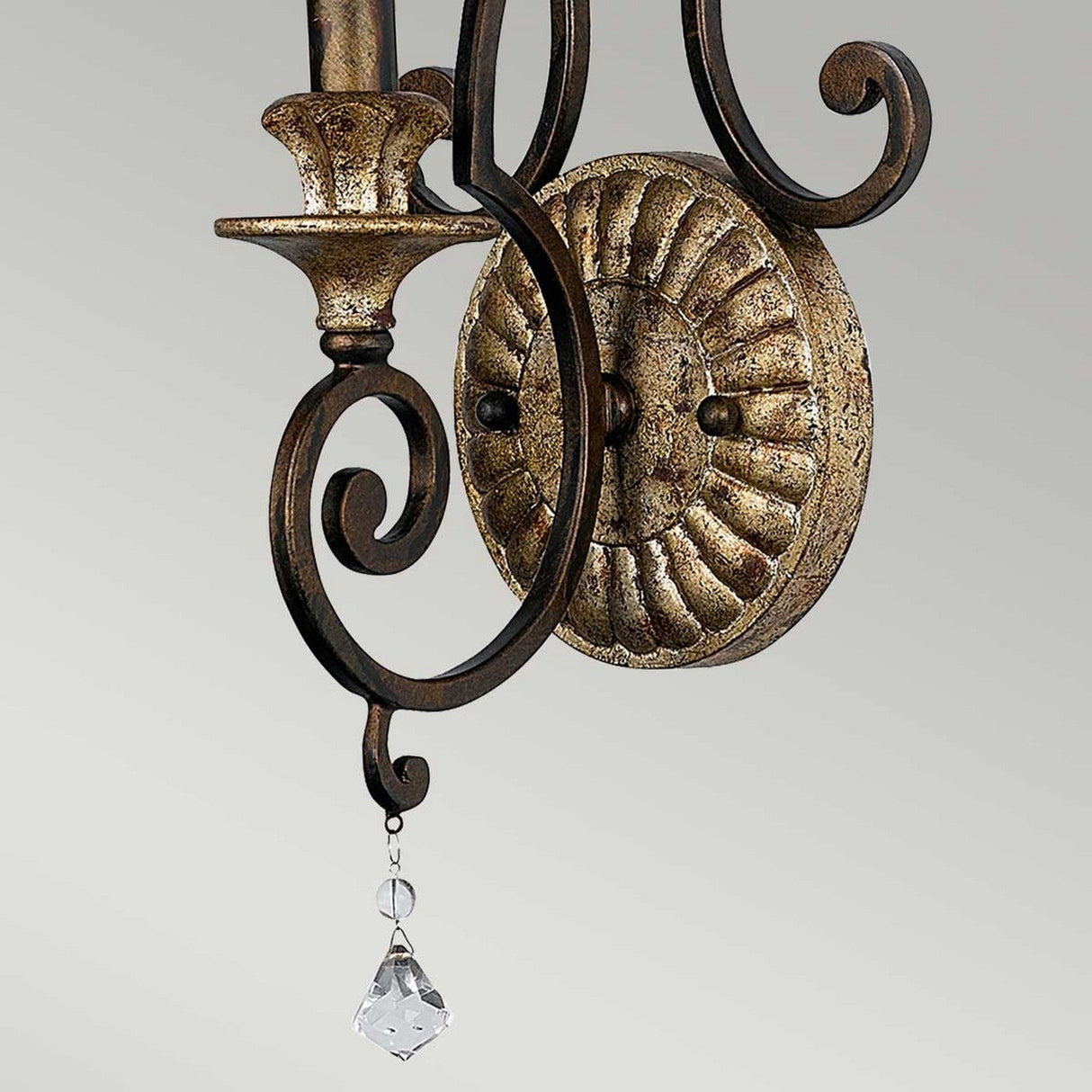 A close-up of the Marquette 1 Light Wall Light in bronze showcases its elaborate scrollwork and dangling crystal drops, shining brightly against a simple light gray background.