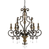 The Marquette 9 Light Chandelier in bronze boasts a dark metal frame embellished with intricate scrollwork and showcases six candle-style lights accompanied by hanging crystal drops, exuding an elegant charm.
