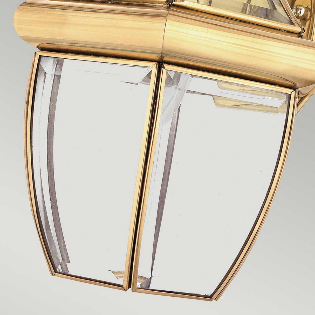 Close-up of the Newbury Outdoor 1 Light Medium Wall Lantern, highlighting its hexagonal design with beveled glass panels. It boasts a lacquered polished brass finish, elegantly set against a light gray background.