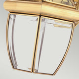 Close-up of the Newbury Outdoor 1 Light Medium Wall Lantern, highlighting its hexagonal design with beveled glass panels. It boasts a lacquered polished brass finish, elegantly set against a light gray background.