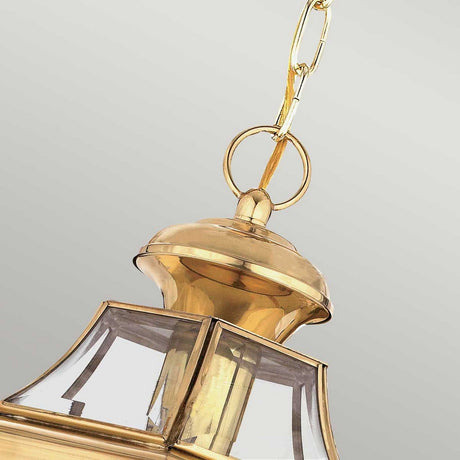 Close-up of the Newbury Outdoor 1 Light Medium Chain Pendant, featuring a hanging brass lantern with clear beveled glass panels and a lacquered polished brass finish. The shiny surface and elegant design of the lantern are showcased against a neutral background.