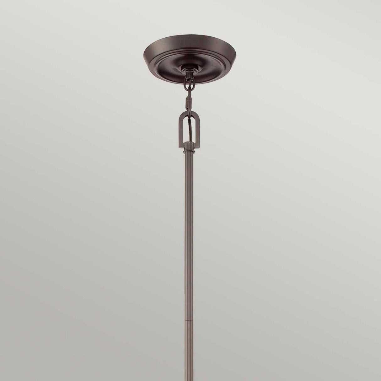 Close-up of the Penn Station 3 Light Chandelier in Western Bronze, ceiling-mounted with a chain link connection against a light grey background. The fixture features an industrial aesthetic with its metallic finish and round base attached to the ceiling, reminiscent of a minimalist chandelier design.