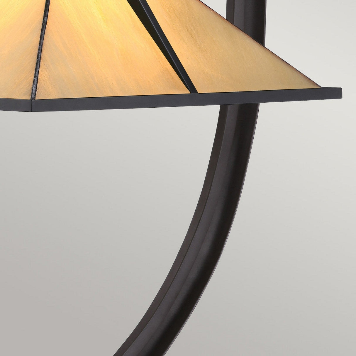 Close-up of the Pomeroy 1 Light Tiffany Table Lamp, showcasing its triangular, warm-toned handcrafted glass shade paired with a sleek black metal frame in a Western Bronze finish. The design features curved lines and geometric shapes, offering a contemporary aesthetic against a neutral background.