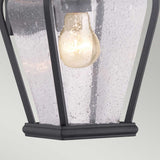 A close-up of the Province 1 Light Wall Lantern in black, featuring seeded glass panels. Crafted from durable cast aluminum, the fixture houses a glowing light bulb within its black metal framework, creating a warm glow.