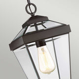 The Ravine Outdoor Medium Chain Pendant in Western Bronze highlights an exposed vintage-style filament bulb with its black metal frame and clear beveled glass panels. The simple yet elegant geometric design adds a modern touch, seamlessly blending style whether used indoors or as an outdoor pendant.