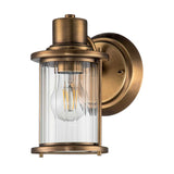 The Riggs 1 Light Wall Light - Weathered Brass is a vintage-inspired wall sconce that features a cylindrical glass shade and an exposed bulb, mounted on a round weathered brass backplate. Its design merges industrial style with classic elements, creating an elegant lighting solution for your bathroom.