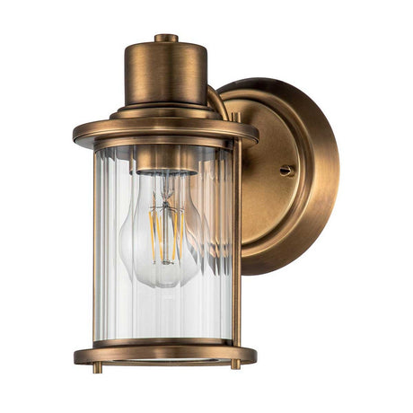 The Riggs 1 Light Wall Light - Weathered Brass is a vintage-inspired wall sconce that features a cylindrical glass shade and an exposed bulb, mounted on a round weathered brass backplate. Its design merges industrial style with classic elements, creating an elegant lighting solution for your bathroom.