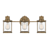Riggs 3 Light Wall Light in Weathered Brass features a trio of ribbed glass shades with exposed bulbs, supported on a horizontal brass bar and secured to a round backplate.