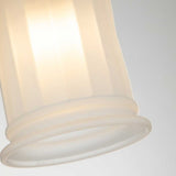 A close-up of the Swell 1 Light Wall Light with a softly glowing, frosted white glass shade. The ambient illumination creates a warm and gentle glow, highlighting the textured surface of the glass. The fixture is adorned with brushed brass, set against a soft, neutral gray background.