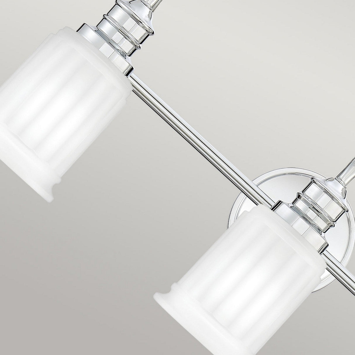 A close-up of the Swell 3 Light Wall Light - Polished Chrome highlights its modern design with two frosted glass shades. The fixture's minimalist style, featuring sleek cylindrical shapes and metallic accents, makes it an elegant addition to chic bathroom vanities.