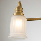 Close-up of the Swell 4 Light Wall Light in brushed brass, showcasing a vintage-style finish with a frosted glass shade and an elegant ribbed design. The softly glowing light exudes metropolitan sophistication against a neutral background.