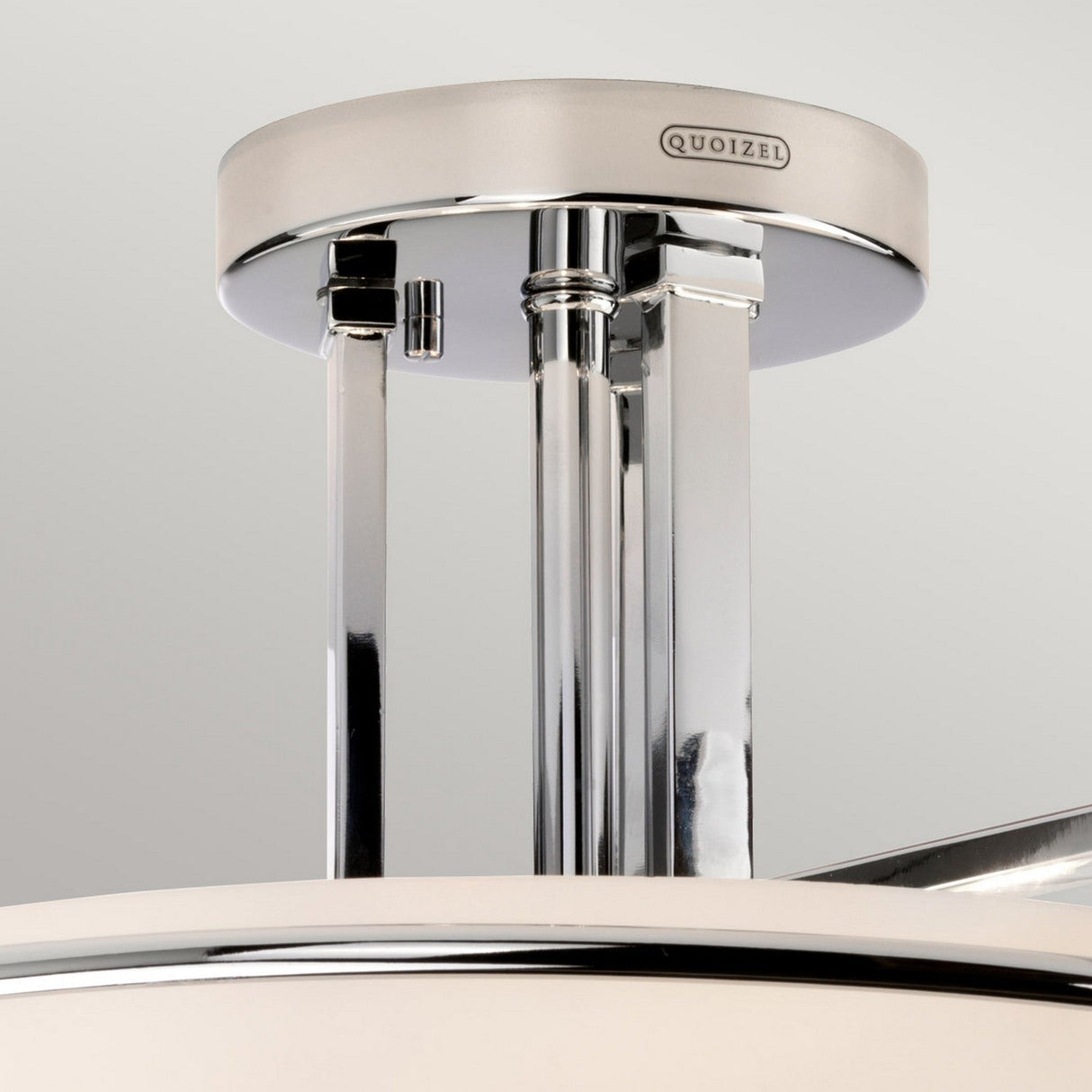 Close-up of a Quoizel Taylor 3 Light Semi-Flush ceiling fixture, featuring a polished chrome finish and opal etched glass. The brand name is visible on the metal plate attached to the white circular mount.