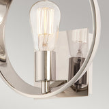 Get a close-up view of the Theatre Row 1 Light Wall Light in Imperial Silver, showcasing its Edison-style bulb with intricate filaments. This fixture features a shiny frame with a circular design, mounted on a reflective square base for an emphasis on its sleek, contemporary style.