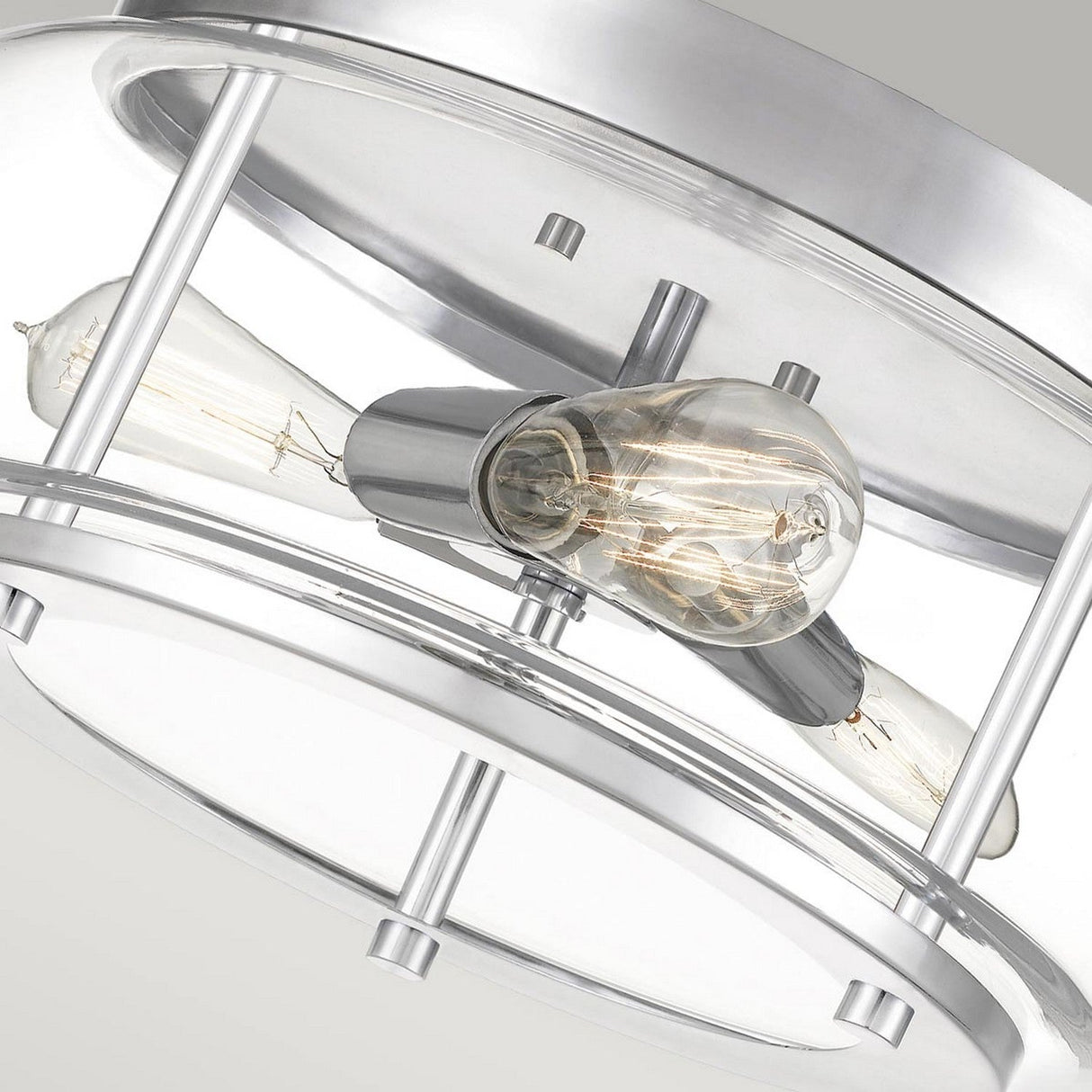 Close-up of the Trilogy 3 Light Flush featuring a sleek, circular metal frame with two exposed Edison-style bulbs. The polished chrome finish is smooth and reflective, enhancing its contemporary look against a neutral background.