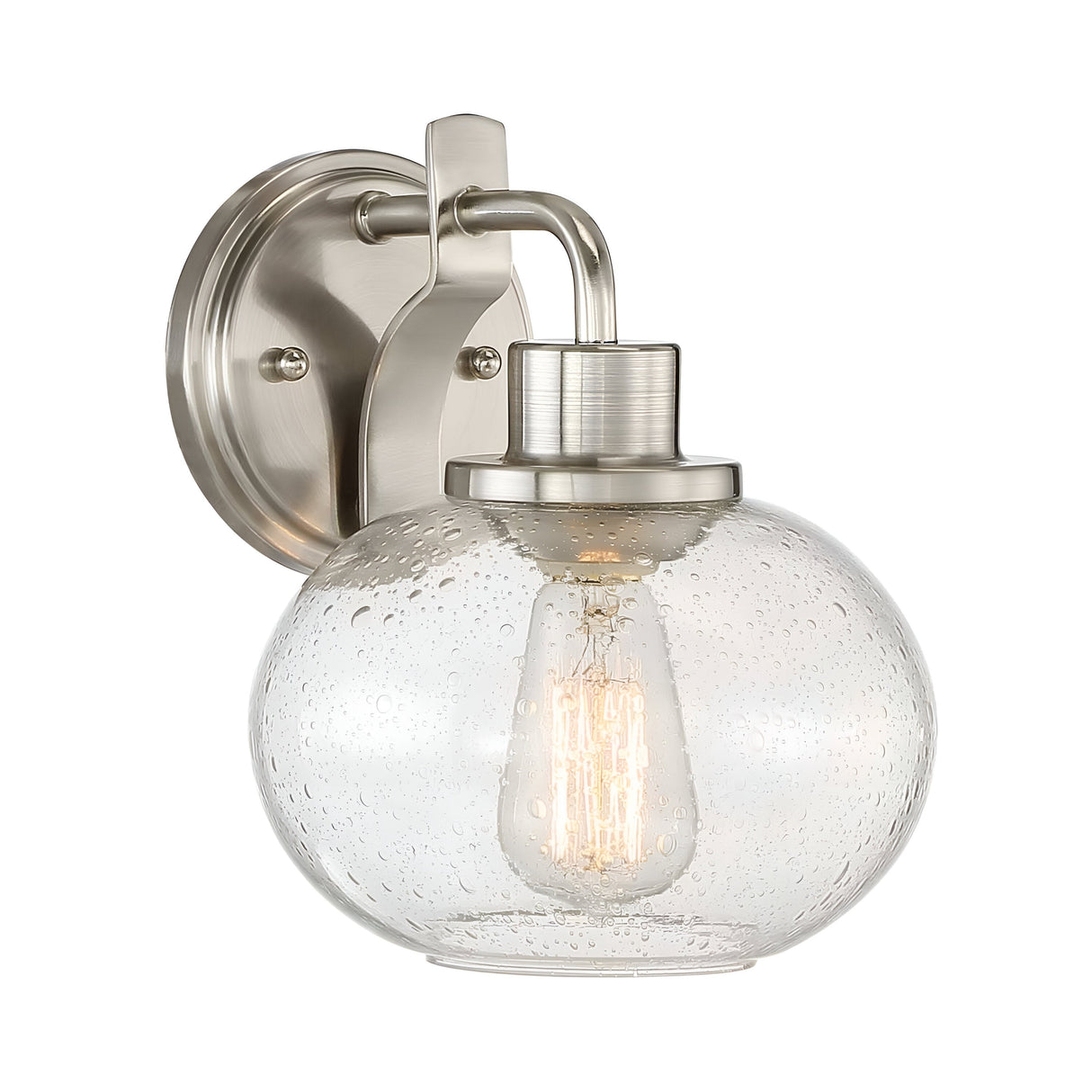 The Trilogy 1 Light Wall Light - Brushed Nickel is a wall-mounted fixture featuring a brushed nickel finish and a clear, globe-shaped seeded glass shade. The textured, bubble-like pattern of the glass beautifully displays an Edison-style bulb inside, offering a modern and elegant design.